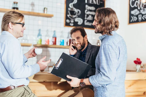 Hombres de negocios trabajando y hablando en la cafetería - foto de stock