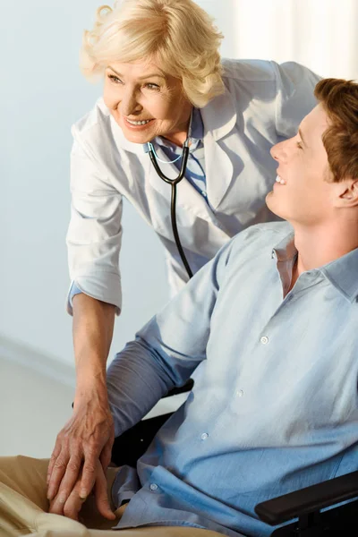 Doctor smiling with young man in wheelchair — Stock Photo