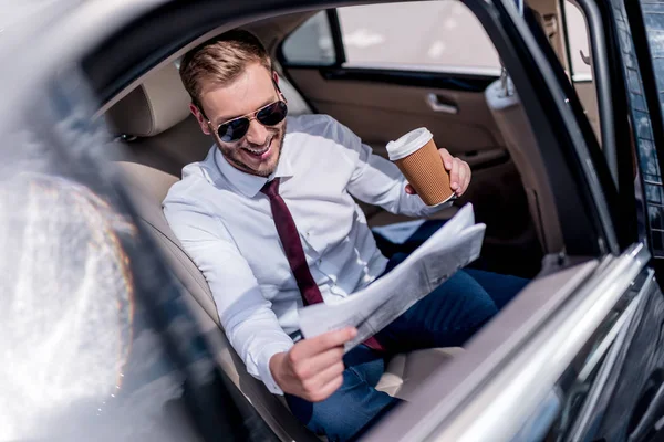 Businessman with coffee and newspaper on backseat — Stock Photo