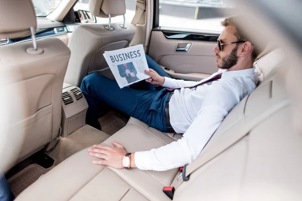 Hombre de negocios con periódico de negocios en el asiento trasero - foto de stock