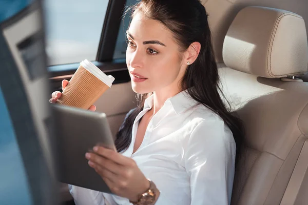 Frau im Auto mit digitalem Tablet und Kaffee — Stockfoto