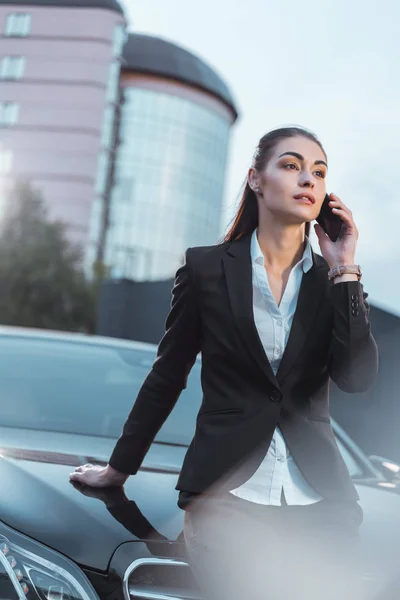 Woman sitting on car and talking on phone — Stock Photo
