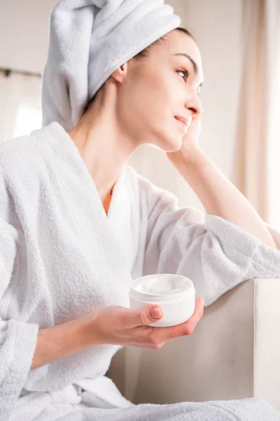 Mujer en albornoz sosteniendo frasco de crema - foto de stock