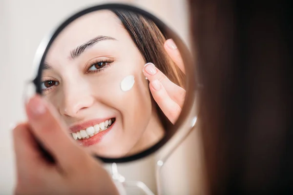 Mujer sonriente aplicando crema facial - foto de stock