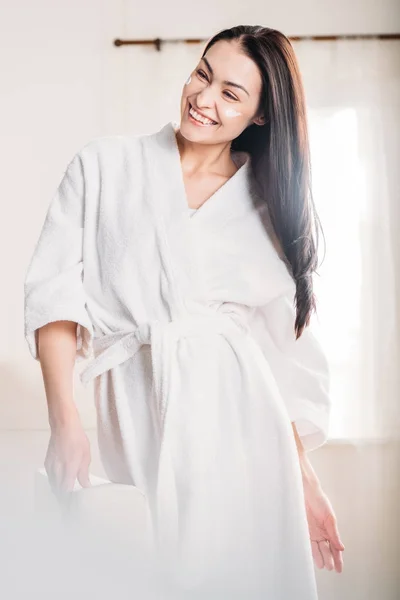 Young woman in bathrobe with cream on face — Stock Photo