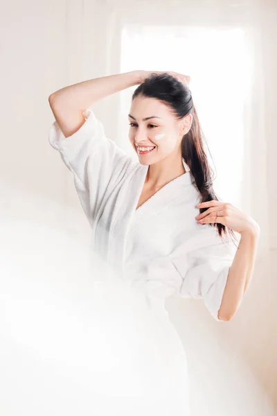 Smiling woman in bathrobe with cream on face — Stock Photo