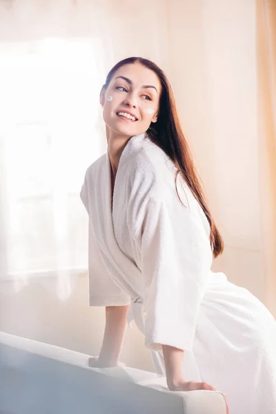 Mujer sonriente en albornoz con crema en la cara — Stock Photo
