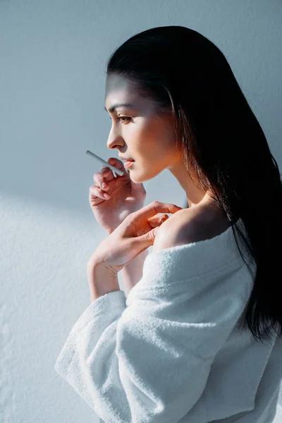 Mujer joven en albornoz fumando - foto de stock