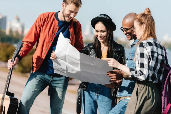 Amigos multiculturales elegir destino en el mapa - foto de stock