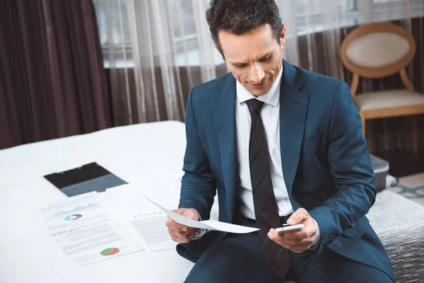 Hombre de negocios sosteniendo el papeleo y el uso de smartphone - foto de stock