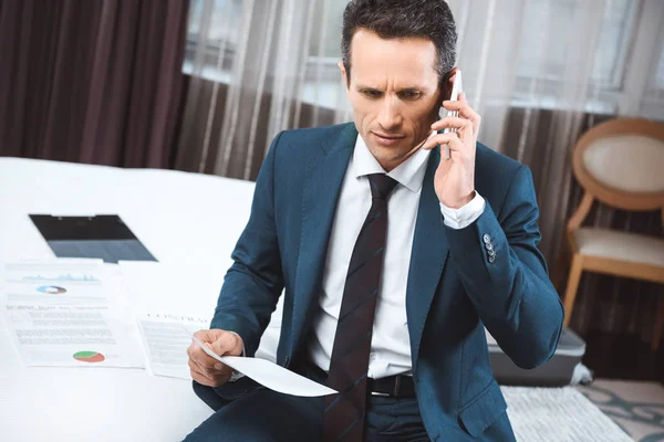 Hombre de negocios sosteniendo papeleo y hablando por teléfono - foto de stock