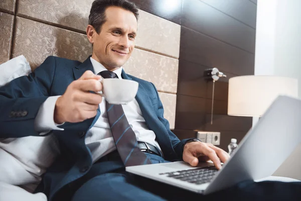 Homme d'affaires au lit avec ordinateur portable et café — Photo de stock