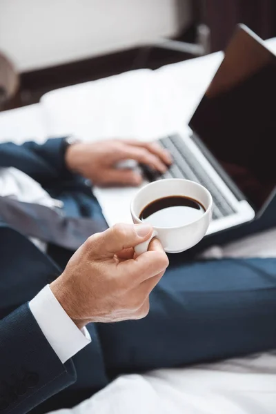 Businessman on bed with laptop and coffee — Stock Photo