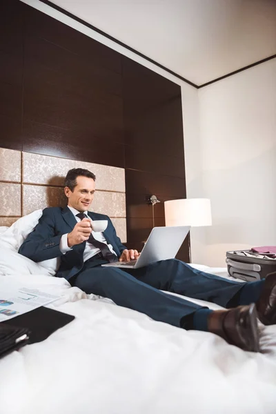 Homme d'affaires au lit avec ordinateur portable et café — Photo de stock