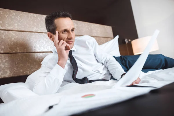 Businessman on bed reading paperwork — Stock Photo