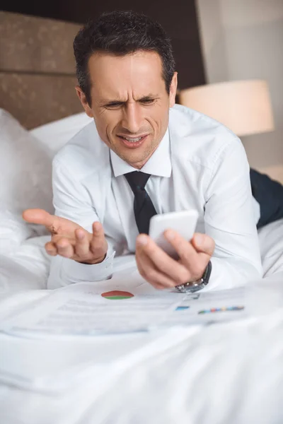 Businessman on bed using smartphone — Stock Photo