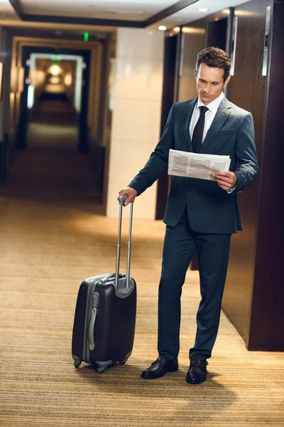 Бизнесмен с чемоданом читает газету — стоковое фото