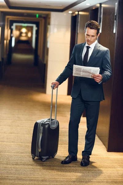 Hombre de negocios con maleta leyendo periódico - foto de stock