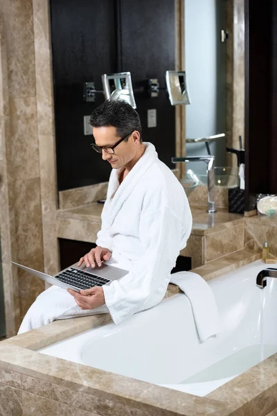 Businessman in bathrobe using laptop — Stock Photo