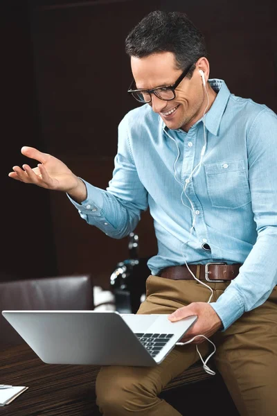 Uomo d'affari ridente in cuffia utilizzando il computer portatile — Foto stock