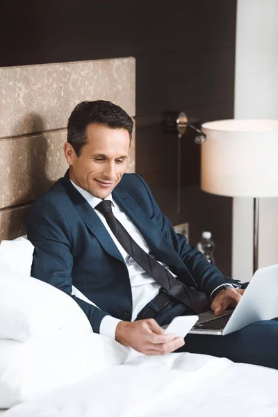 Businessman on bed with smartphone and laptop — Stock Photo