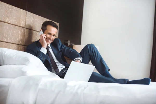 Hombre de negocios en la cama con ordenador portátil y teléfono - foto de stock