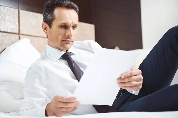 Businessman on bed reading paperwork — Stock Photo