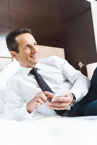 Businessman on bed using smartphone — Stock Photo