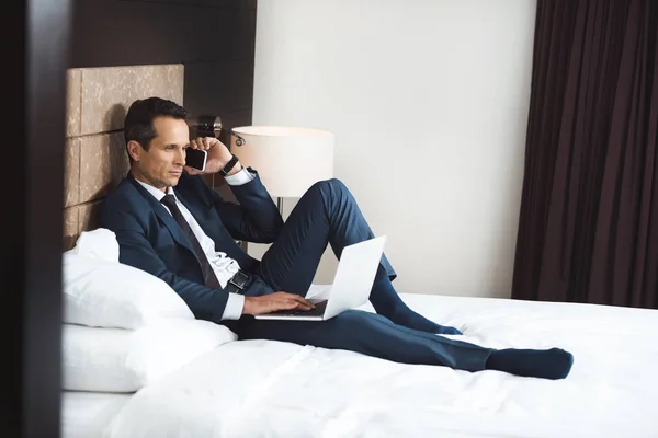 Бизнесмен на кровати с телефоном и ноутбуком — стоковое фото