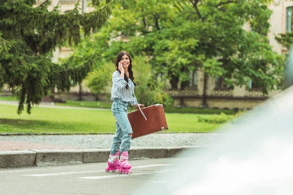 Дівчина в роликових ковзанах зі смартфоном і валіза — стокове фото