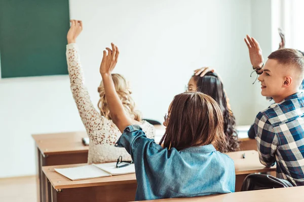 Estudantes levantando as mãos em sala de aula — Fotografia de Stock