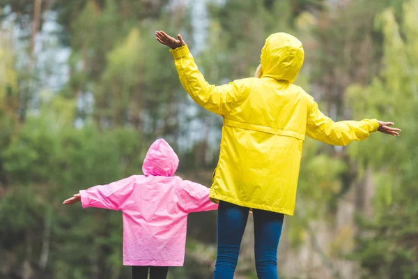 Familia en impermeables con los brazos extendidos - foto de stock