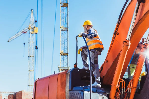 Trabalhador da construção civil em cima da cabine da escavadeira — Fotografia de Stock