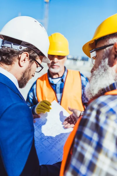 Constructores y hombres de negocios discutiendo planes de construcción - foto de stock