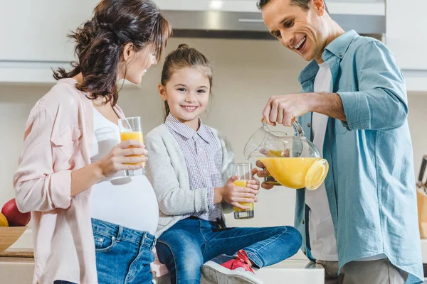 Familia feliz, padre vertiendo jugo en vidrio para la hija en la cocina - foto de stock
