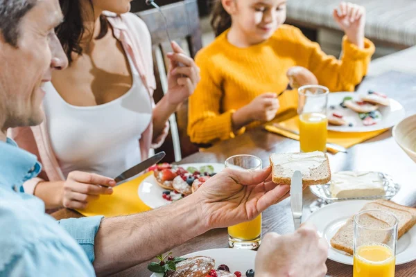 Happy family sitting at table and eating pancakes with berries and juice — Stock Photo