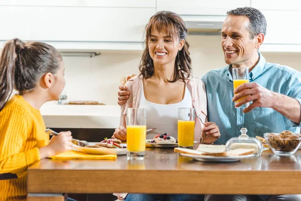 Веселая семья сидит за столом и держит стаканы с соком на кухне — стоковое фото
