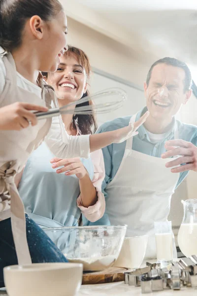 Alegre familia en la cocina, niño tocando la cara de los padres y sosteniendo batidor - foto de stock