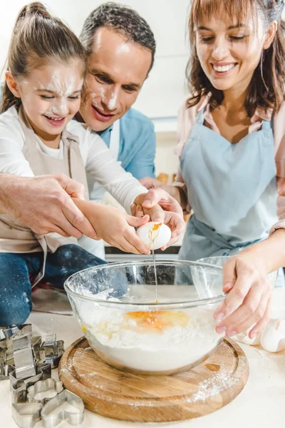 Обрезанный образ счастливой семьи, разделяющей яйцо в миске на кухне — стоковое фото