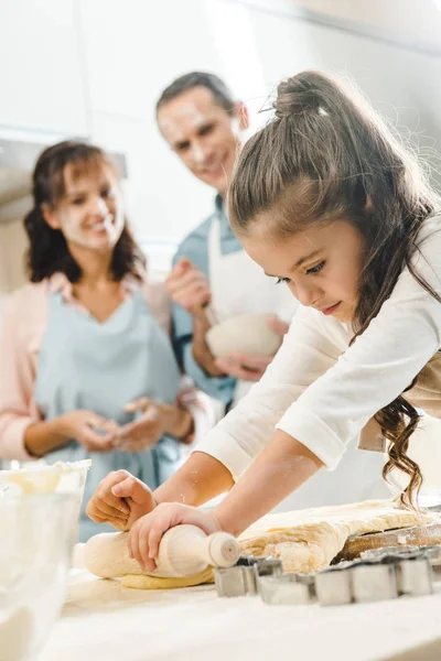 Genitori guardando come grave figlioletta stendere pasta in cucina — Foto stock