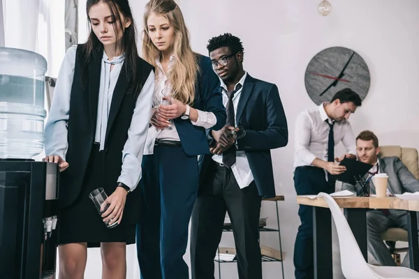 Tired businesspeople standing in queue for water dispenser at office — Stock Photo