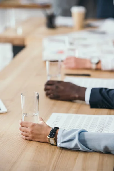 Tiro cortado de empresários sentados com copos de água na sala de conferências — Fotografia de Stock