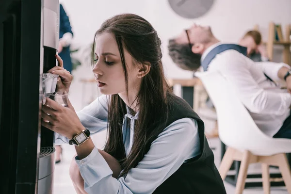 Mulher de negócios exausta derramando água do dispensador em copo de plástico no escritório — Fotografia de Stock