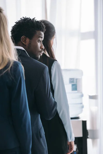 Jeune beau gestionnaire afro-américain debout dans la file d'attente pour distributeur d'eau au bureau — Photo de stock