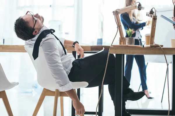 Joven empresario sobrecargado de trabajo durmiendo en la silla en el lugar de trabajo — Stock Photo
