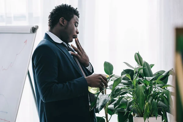 Schläfriger afrikanisch-amerikanischer Geschäftsmann gießt Pflanze im Büro — Stockfoto