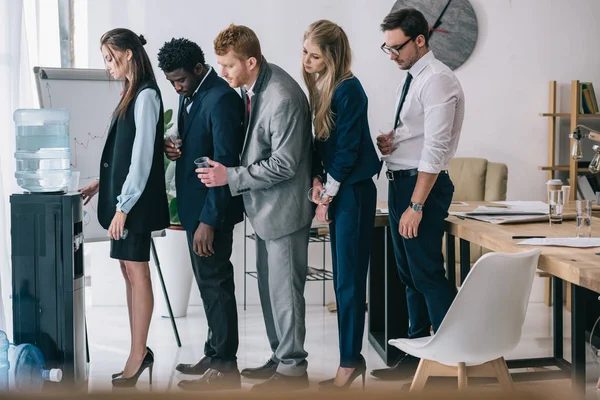 Side view of businesspeople standing in queue for water dispenser at office — Stock Photo