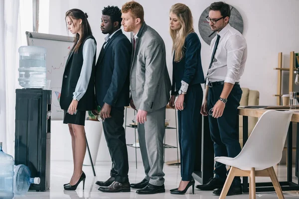 Seitenansicht von Geschäftskollegen, die vor dem Wasserspender im Büro Schlange stehen — Stockfoto