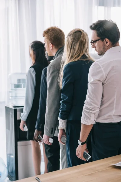Overworked managers standing in queue for water dispenser at office — Stock Photo