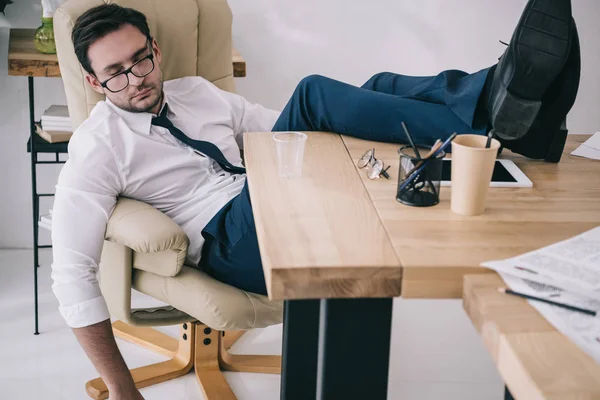 Geschäftsmann schläft im Sessel mit Füßen auf Tisch im Büro — Stockfoto